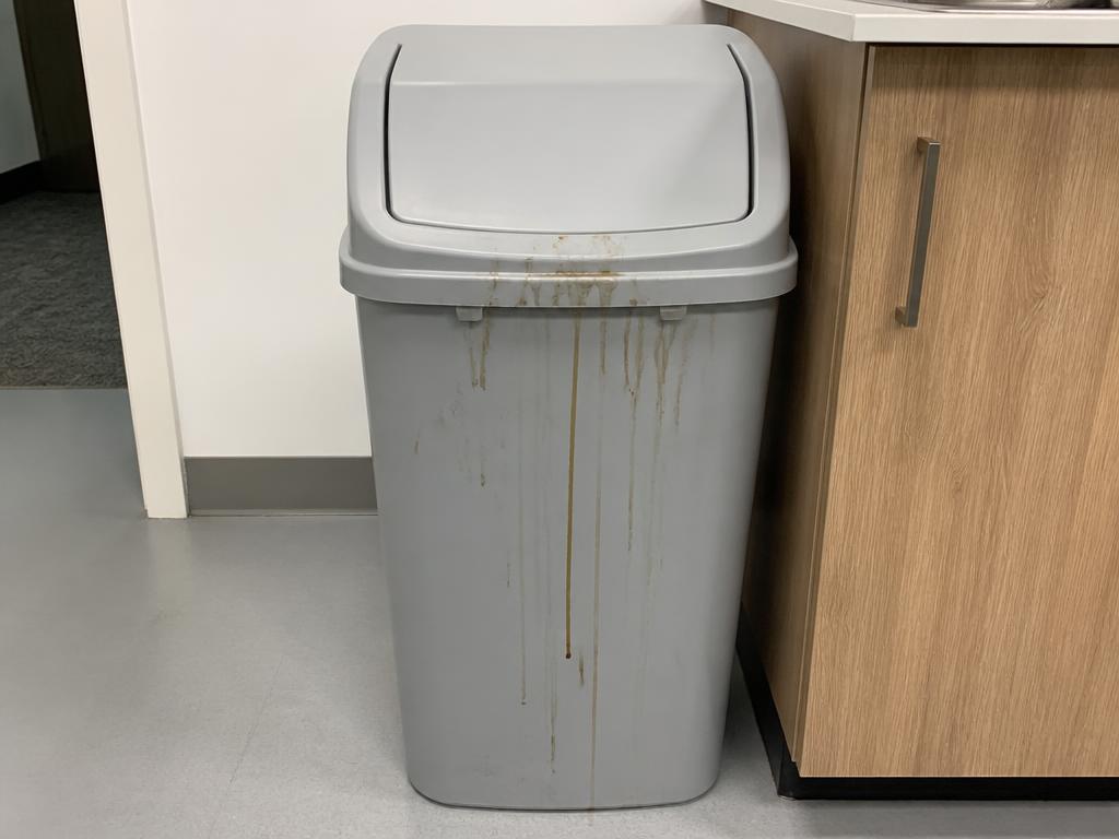 Grey office kitchen waste bin with dried brown spill streaks down the front exterior